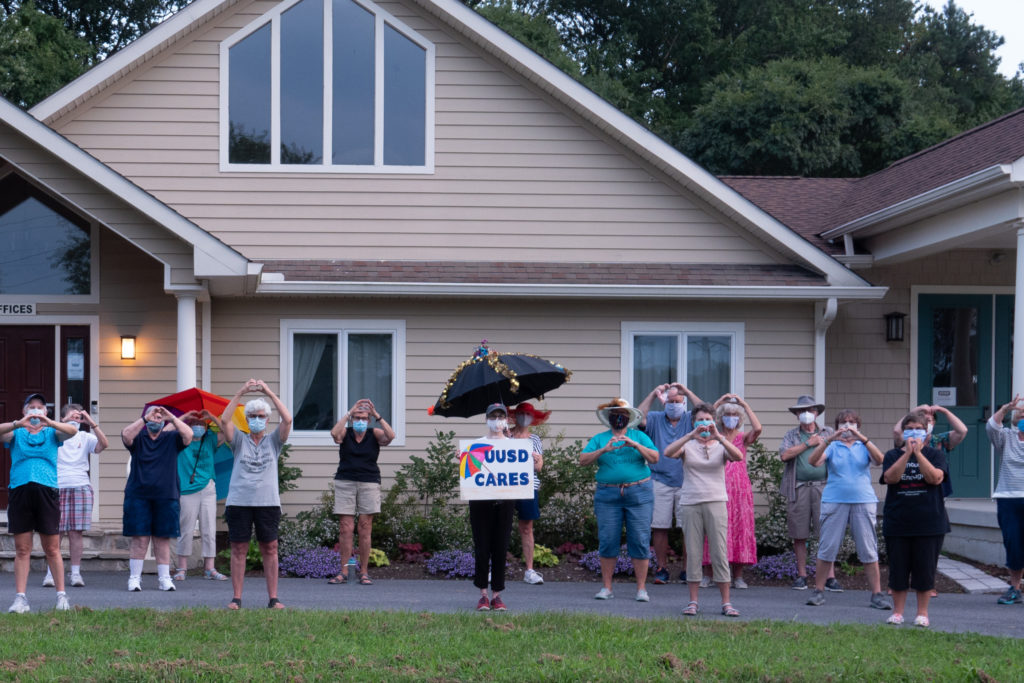 Members of UUSD Cares holding up the heart sign and standing in front of UUSDt