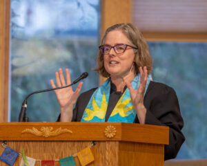 Rev. Heather at the podium with her hands raised.