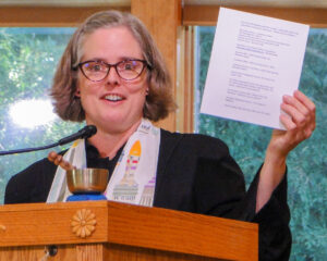 Rev. Heather at the podium holding up a list of labyrinths.